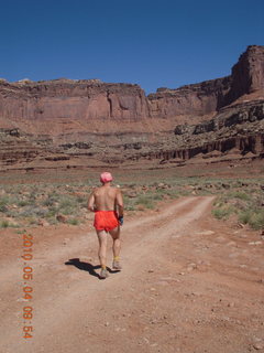 97 774. Canyonlands Lathrop Trail hike - Adam running on white rim road - back
